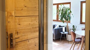 Una porta in legno che dà su una stanza con un tavolo da pranzo, sedie, un divano e una pianta in vaso.