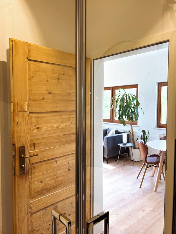 A wooden door leading to a room with a dining table, chairs, a sofa, and a potted plant.
