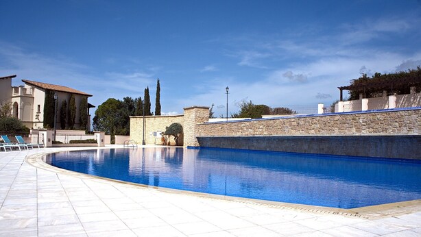 En swimmingpool med en mur av sten och en byggnad med ett tak täckt av tegelpannor.