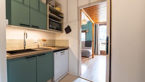 A compact kitchen with a dishwasher, a sink, and a microwave. There is a door leading to a living area with a sofa and a hanging light fixture. - Nice apt for 6 people near the slopes (Morillon)
