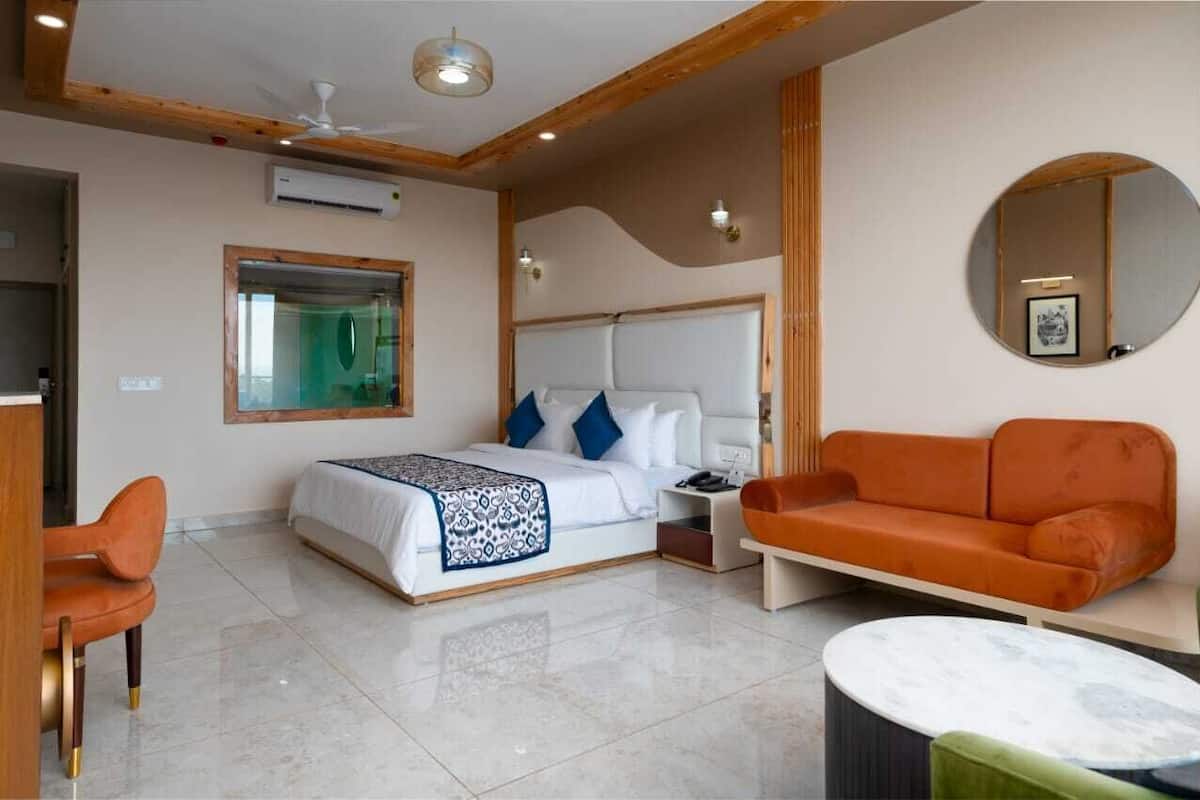 A modern hotel room with a large bed, an orange sofa, a round mirror, and a small table.