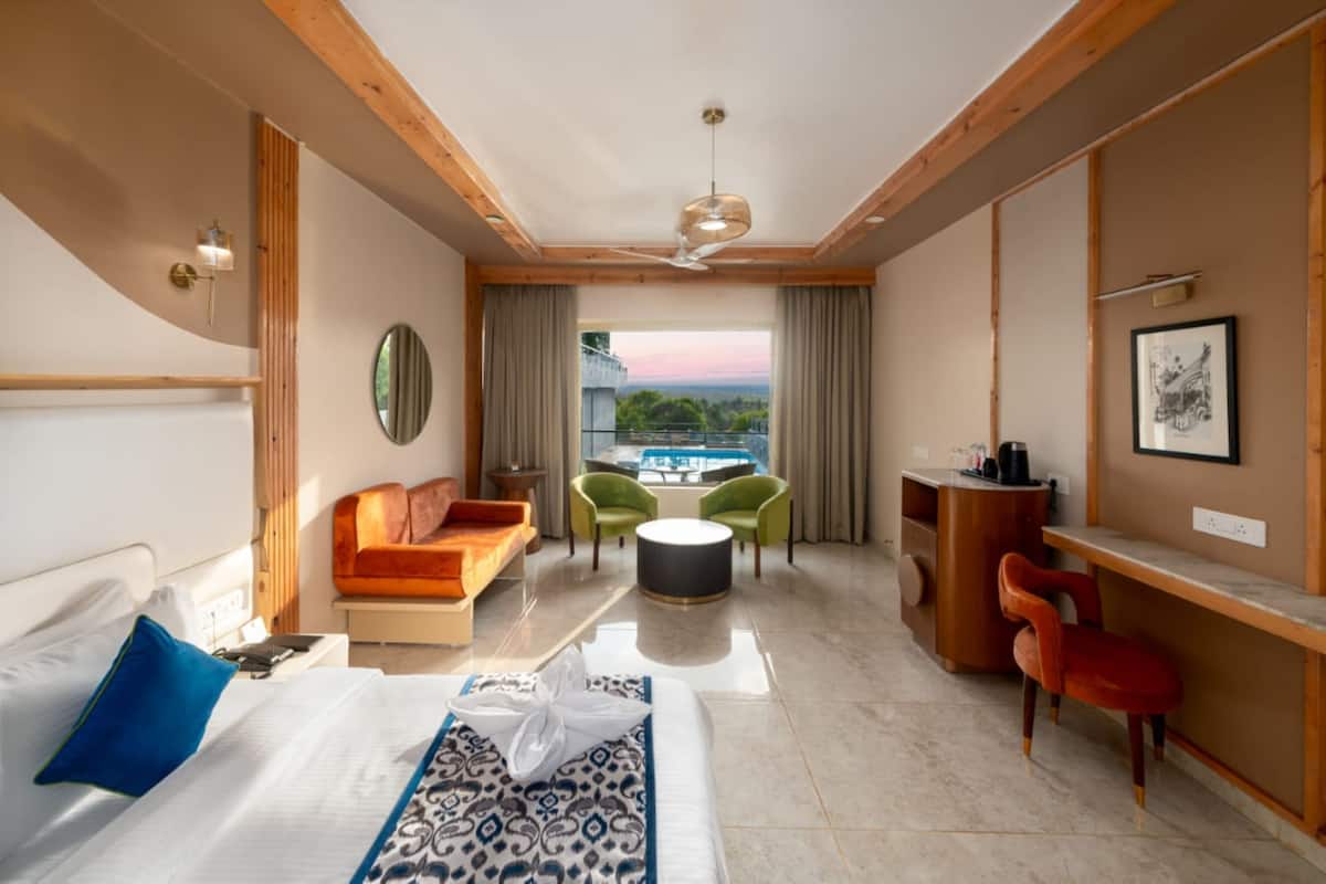 A modern hotel room with a bed, a sofa, a desk, and a balcony with a view.