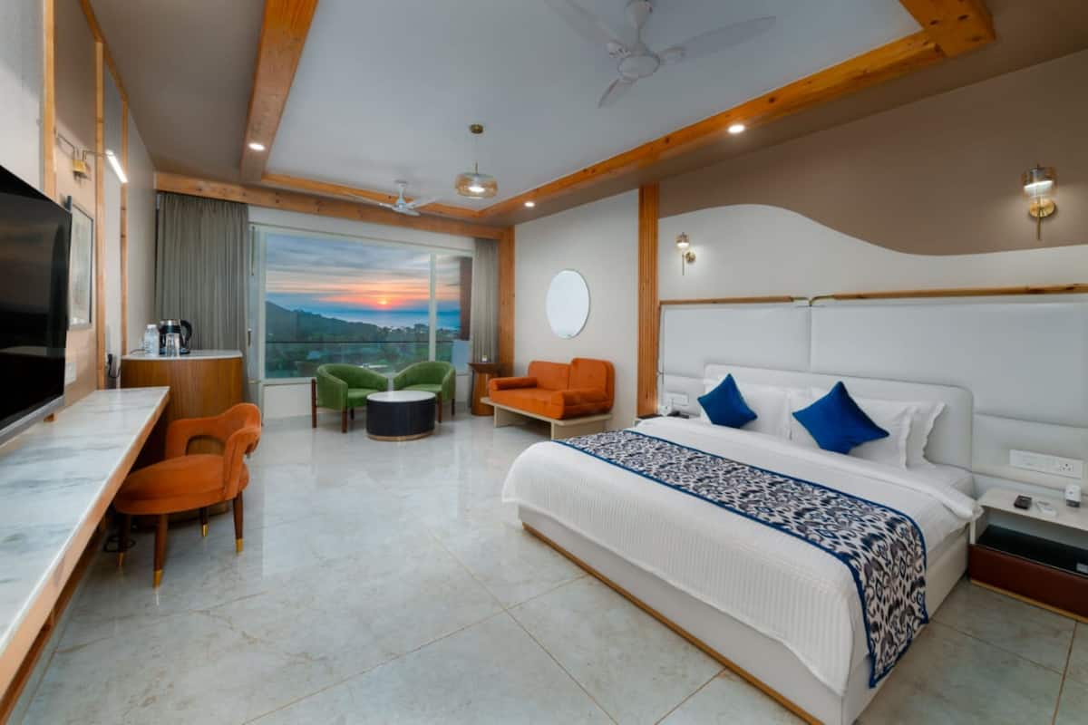 A modern hotel room with a large bed, a desk, and a view of the mountains.