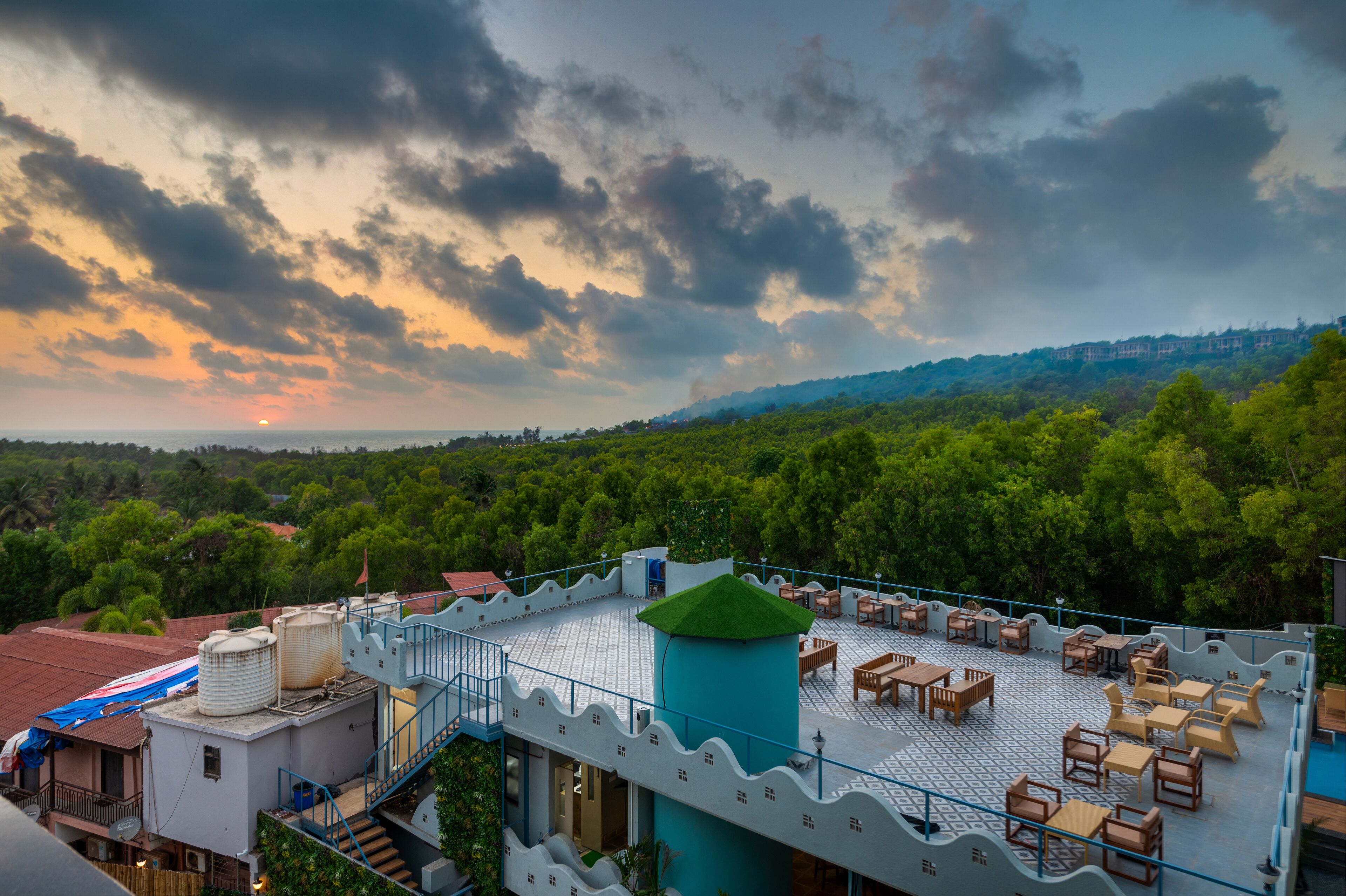 A rooftop terrace with outdoor seating, a water tank, and a view of a forested hill.