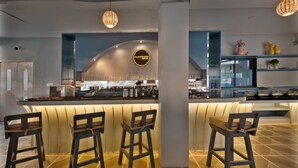 Un área de bar moderna con una barra curva, taburetes y lámparas colgantes.