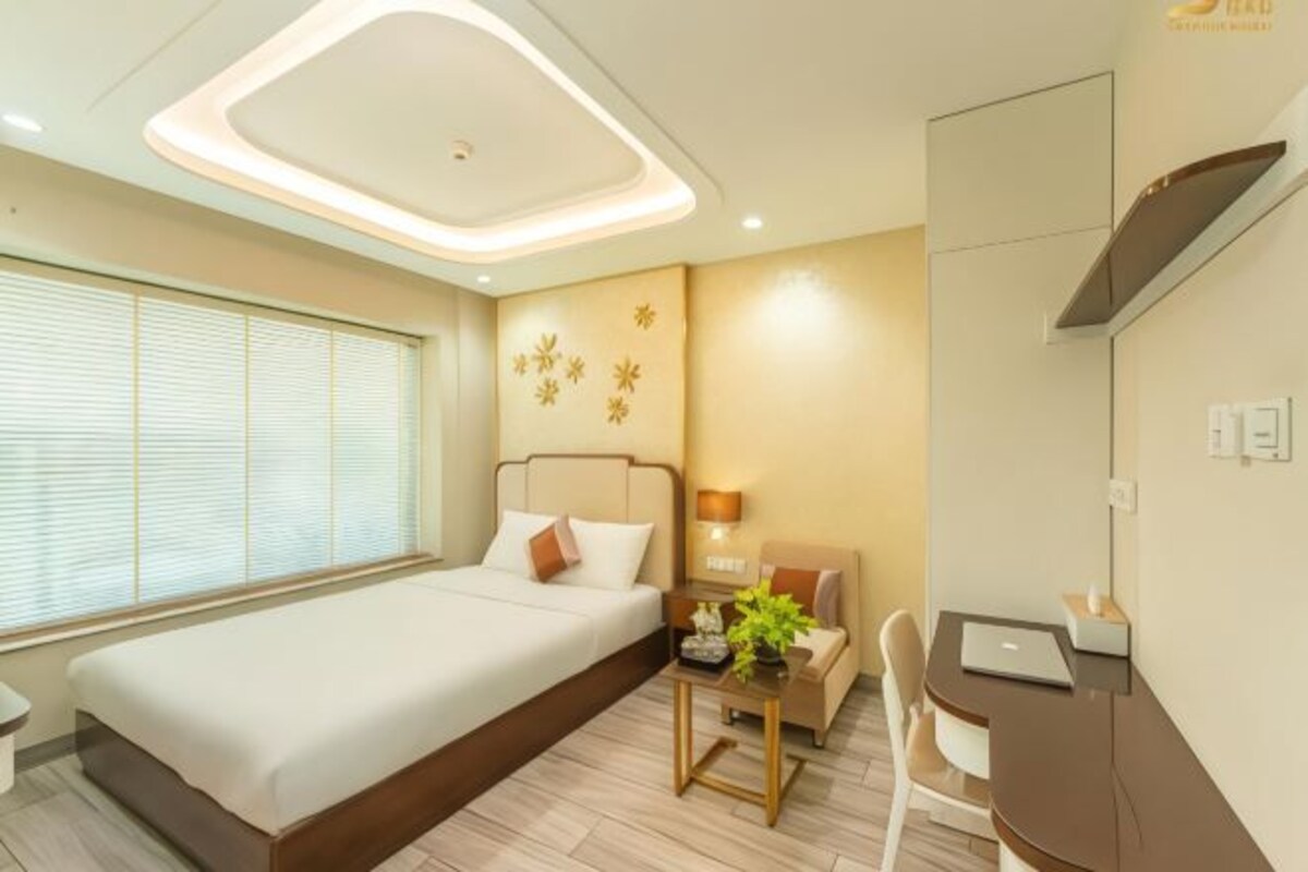 Quarto de hotel moderno com uma cama grande, uma escrivaninha, uma cadeira e uma pequena mesa com uma planta.