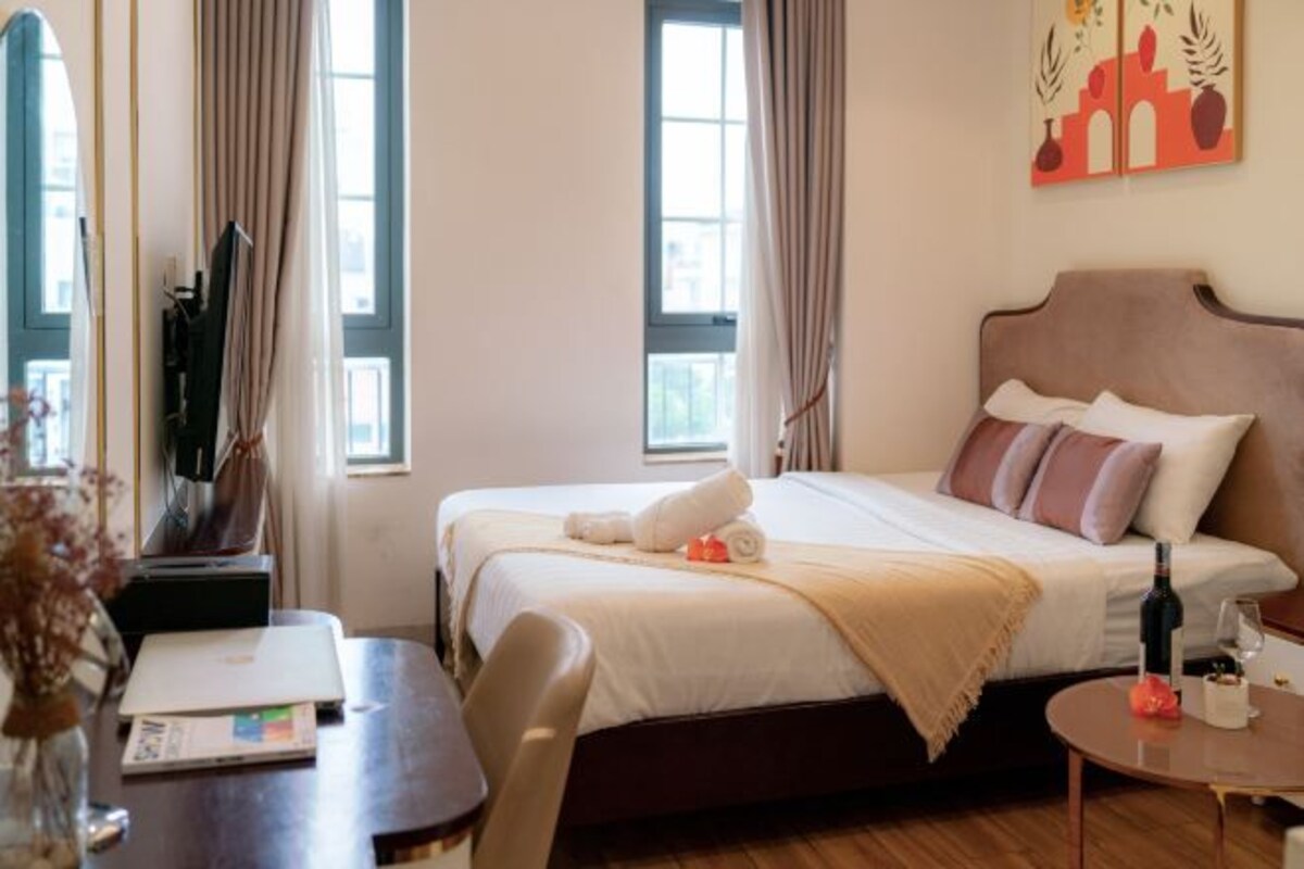Quarto de hotel com cama, escrivaninha, cadeira, mesinha e um quadro na parede.