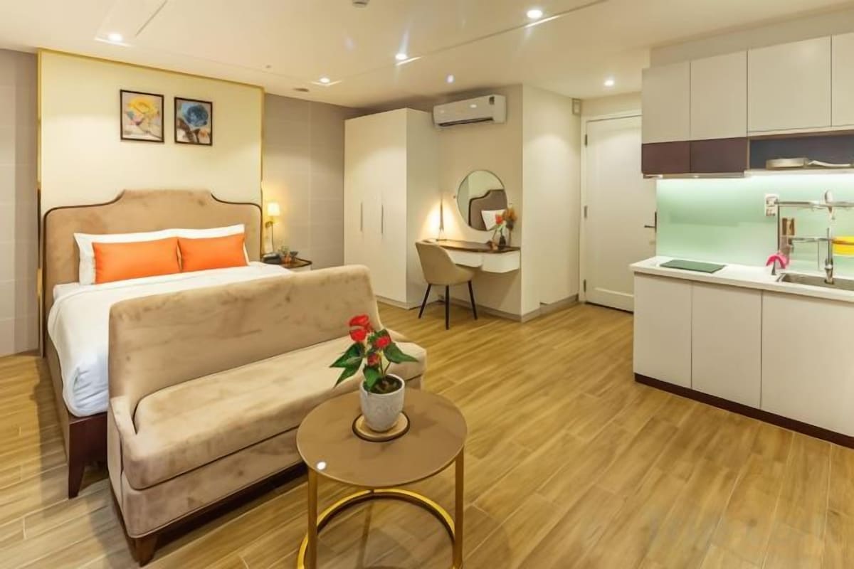 Une chambre d’hôtel comprenant un lit, un canapé, une petite table avec une plante, un bureau avec une chaise et une kitchenette.