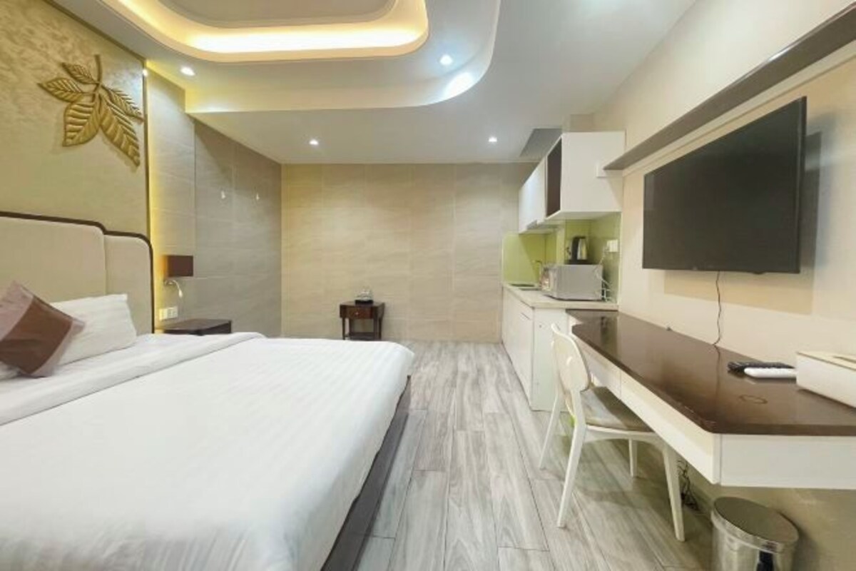 Quarto de hotel moderno com cama, escrivaninha, televisão e uma pequena copa.