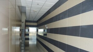 A hallway with a striped wall pattern, a glass elevator, and a door at the end. - Orlando LEK (Benicarló)