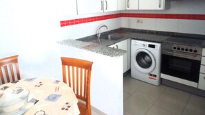 A compact kitchen with white cabinets, a washing machine, and a stove. - Orlando LEK (Benicarló)