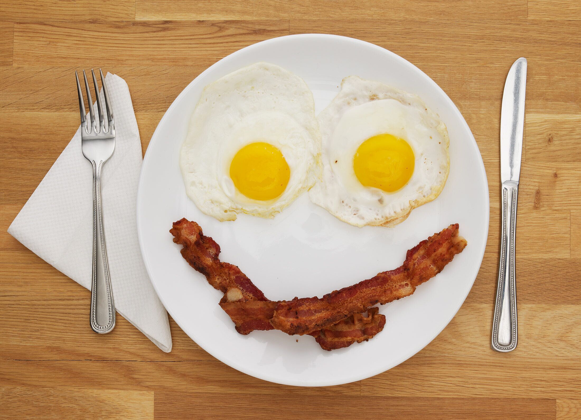 A plate with two fried eggs and a strip of bacon arranged to resemble a smiley face.