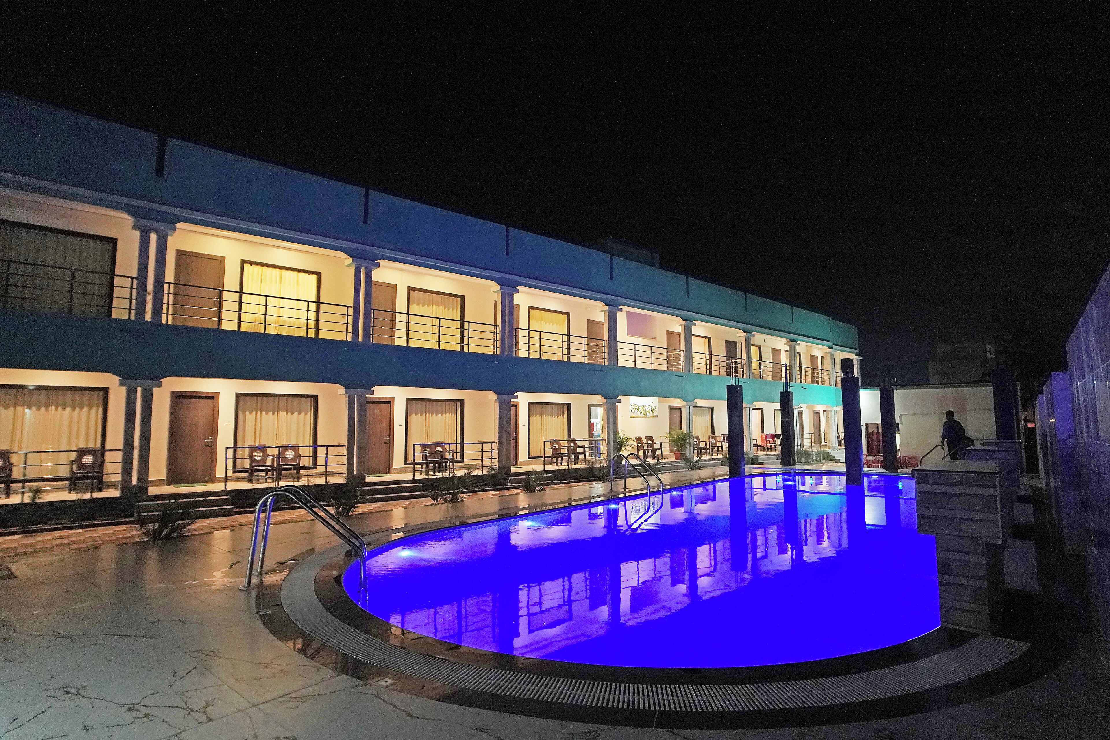 A hotel with a swimming pool at night, featuring a blue-lit pool area and multiple rooms with balconies.