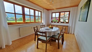 A dining area with a round table, wooden chairs, and a view of the outdoors through large windows.