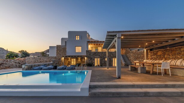 A modern pool area with a stone building, outdoor seating, and a covered patio. - Waterfront Villa Angelika Pink Pelikan (Mykonos)
