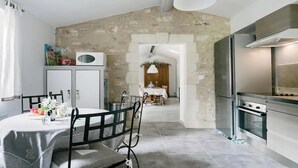 A modern kitchen with a stone wall, a dining area with a round table, and a view into a living room. - TRANQUIL RETREAT: DISCOVER PICTURESQUE COUNTRYSIDE FARMHOUSE WITH POOL (Ménerbes)