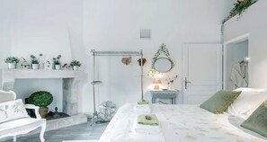 Een slaapkamer met een bed, nachtkastje, lamp, spiegel en open haard.