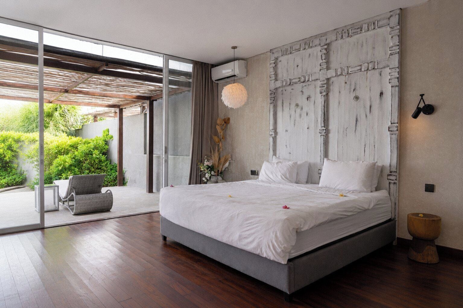 A modern bedroom with a large bed, a sliding glass door to a balcony, and a minimalist decor style.