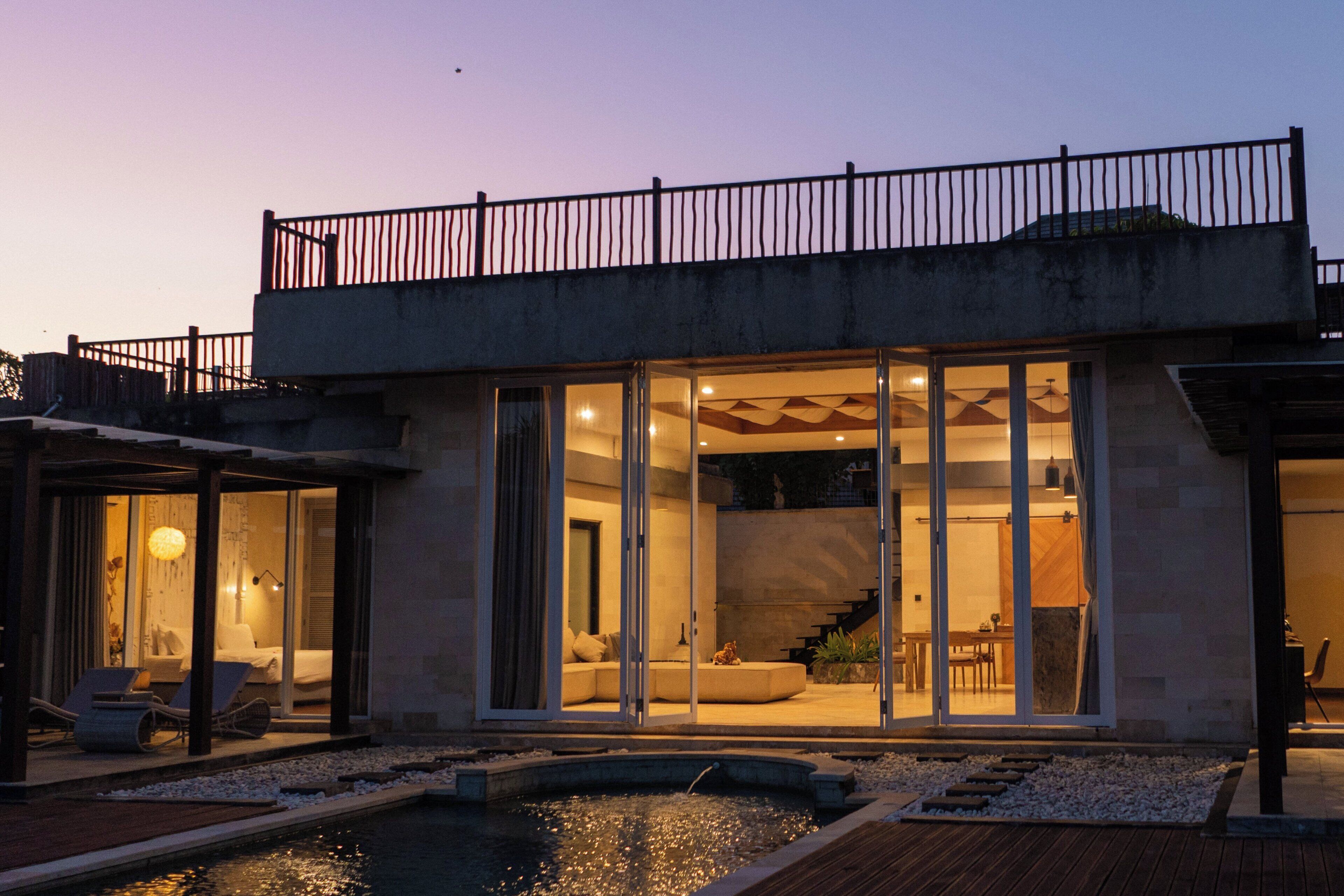 A modern house with a swimming pool, large glass doors, and a balcony.