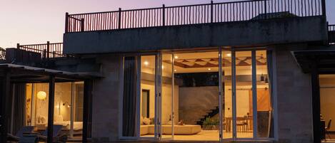 A modern house with a swimming pool, large glass doors, and a balcony.