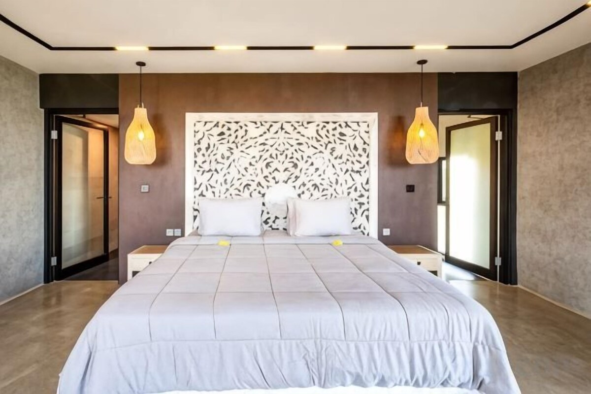 A modern bedroom with a large bed, two bedside tables, a patterned headboard, and pendant lighting.
