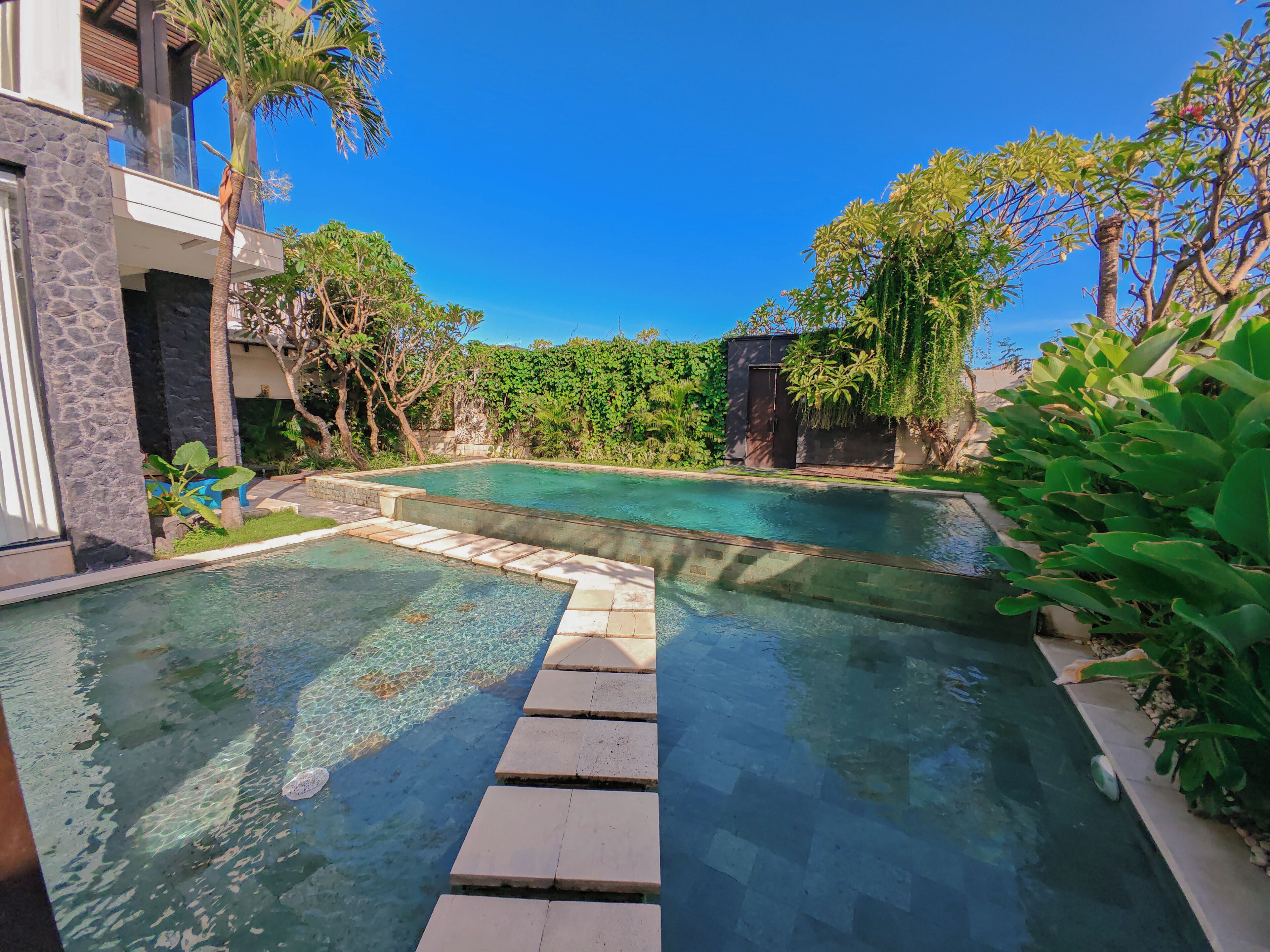 Una piscina con agua cristalina, rodeada de exuberante vegetación y un edificio de piedra.