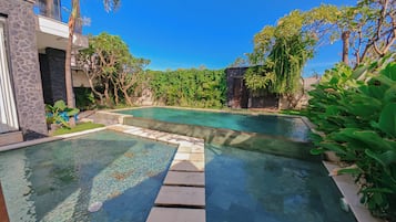 Una piscina con agua cristalina, rodeada de exuberante vegetación y un edificio de piedra.