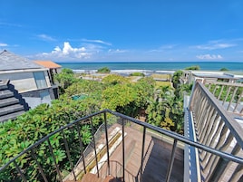 Zona residencial con vista al océano, que cuenta con una terraza de madera y una escalera que conduce a un balcón.