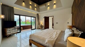 A modern bedroom with a large bed, a television, and a sliding glass door leading to a balcony. - Ketewel Beach Villas & Spa (Batubulan)
