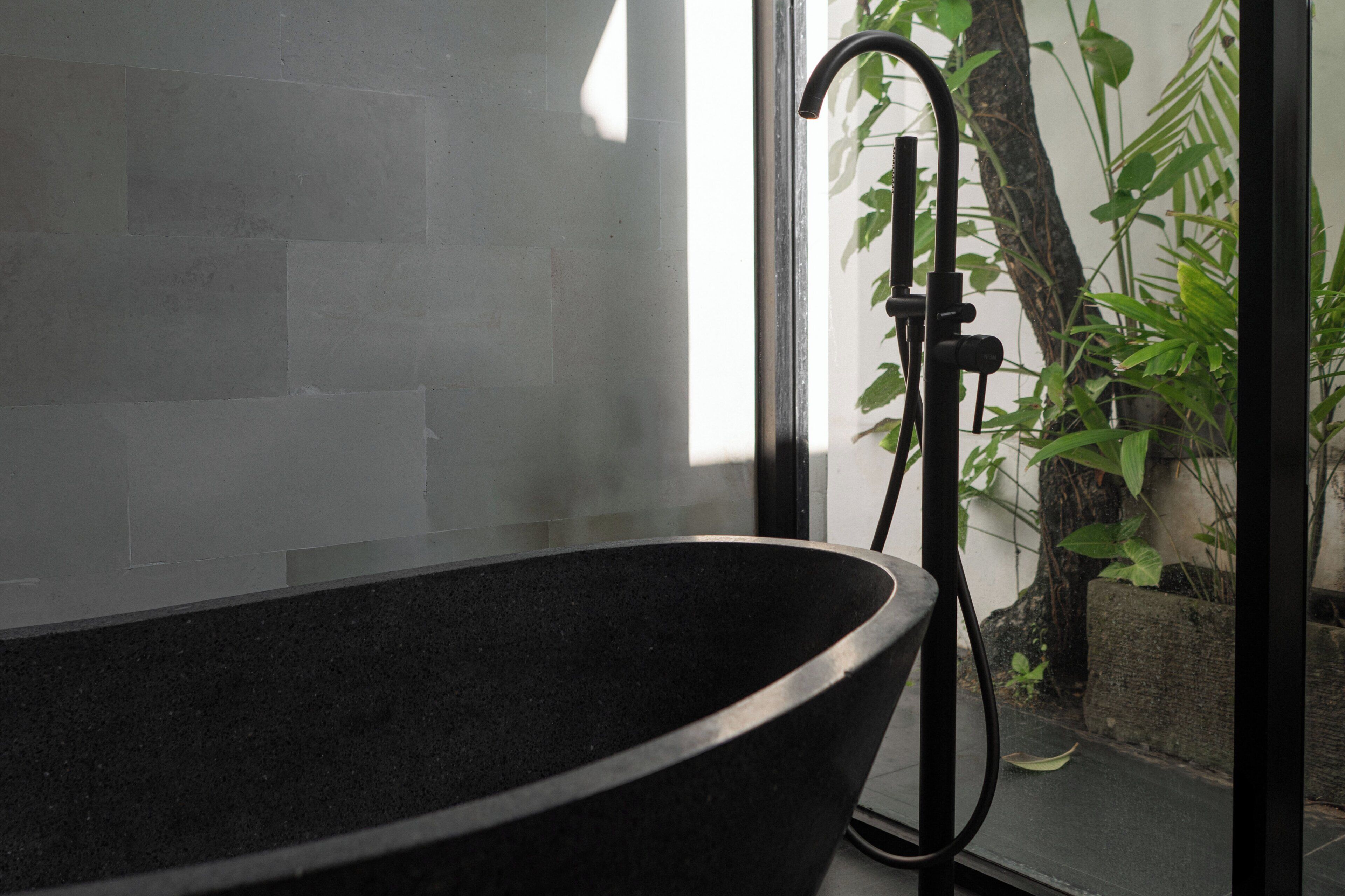 A bathtub with a black interior, positioned next to a window with a view of greenery outside.