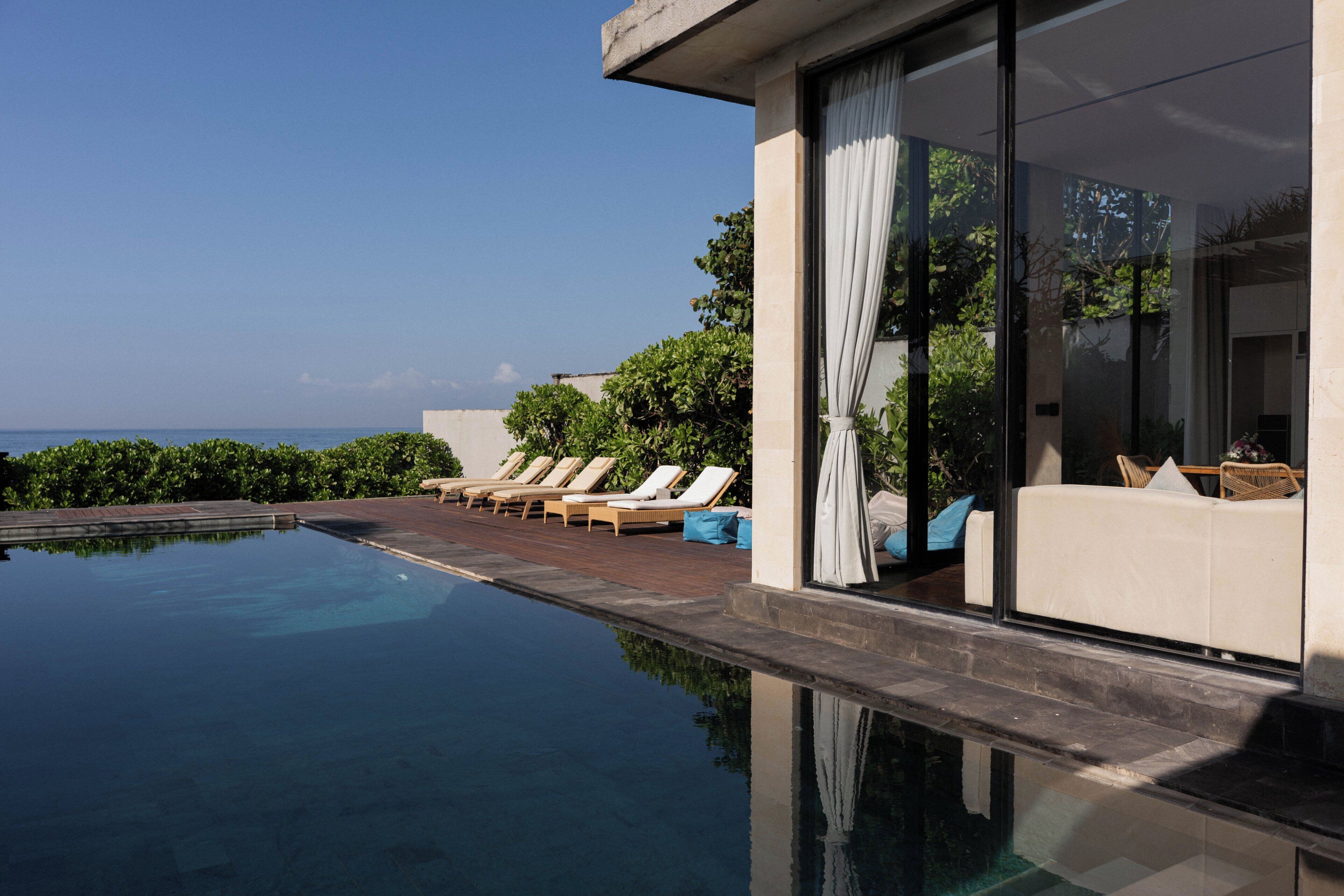 Una piscina infinita moderna con sillones de descanso y vista al océano.