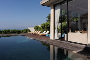 A modern infinity pool with lounge chairs and a view of the ocean.