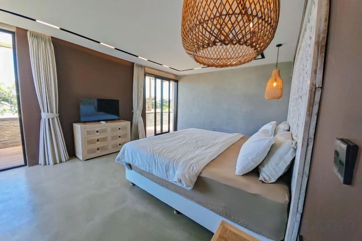 A bedroom with a bed, a dresser, a television, and a large window.