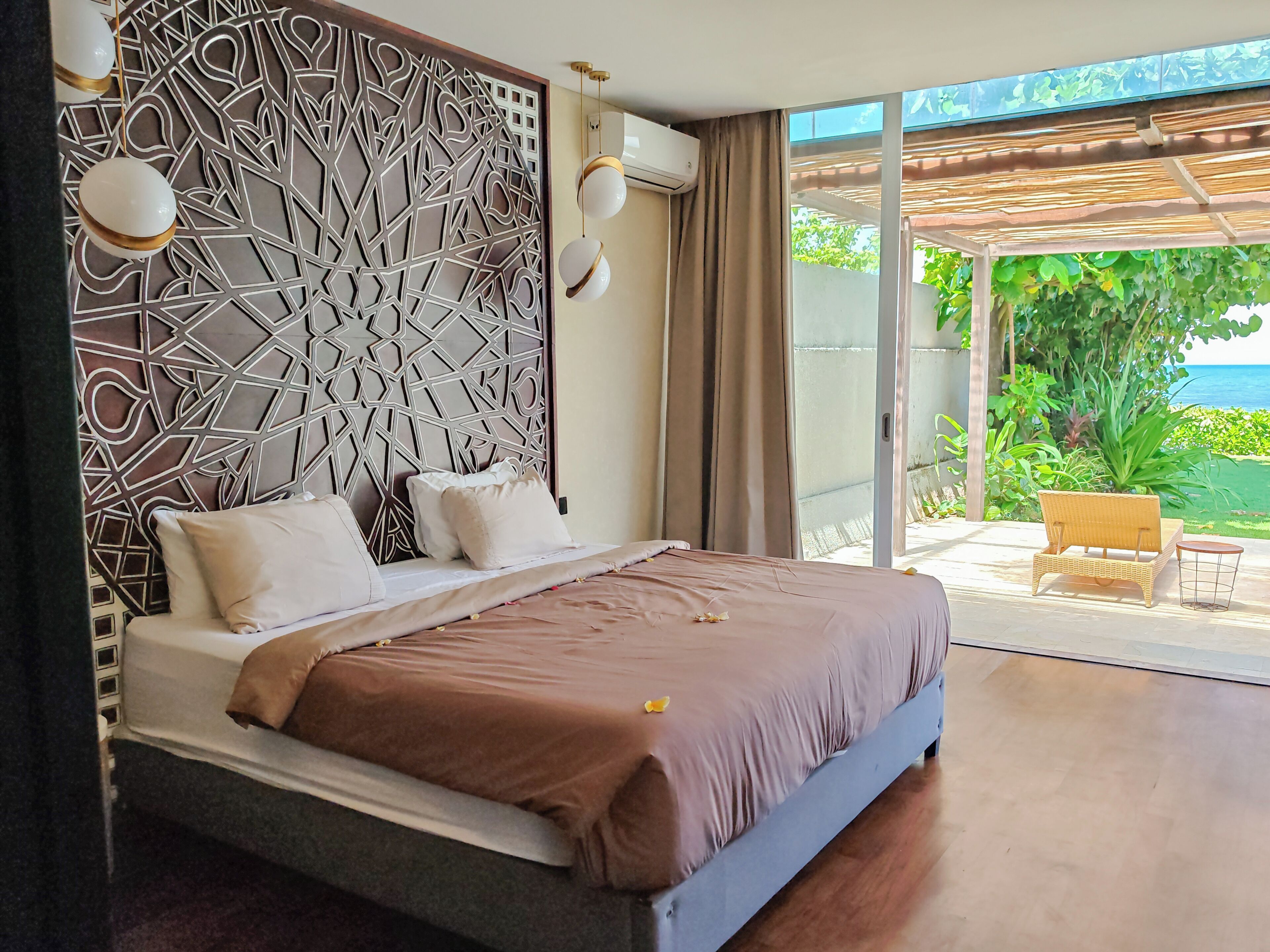 Un dormitorio con una cama grande, un cabecero decorativo y vistas a un jardín y al océano a través de una puerta corredera.