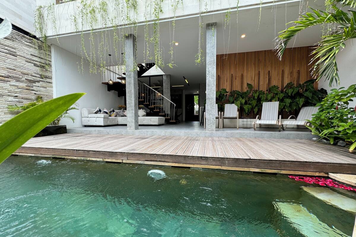 A modern outdoor pool area with a wooden deck, lounge chairs, and hanging plants.