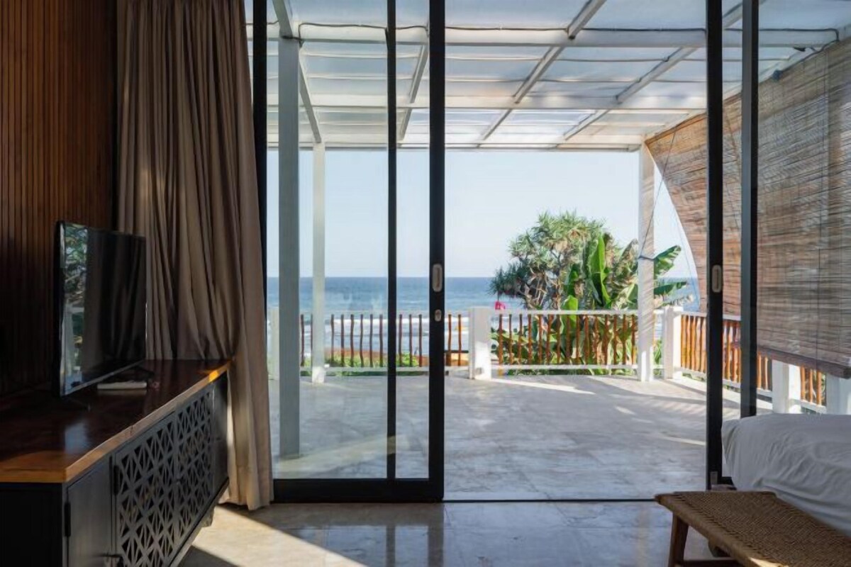 Una habitació amb una porta corredissa de vidre que dona a un balcó amb vista al mar.