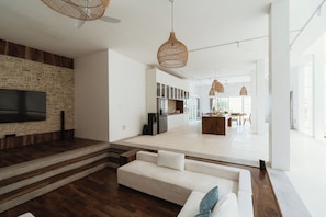 Un salon moderne avec un téléviseur à écran plat fixé à un mur en briques, un canapé blanc et un escalier menant à un espace cuisine.