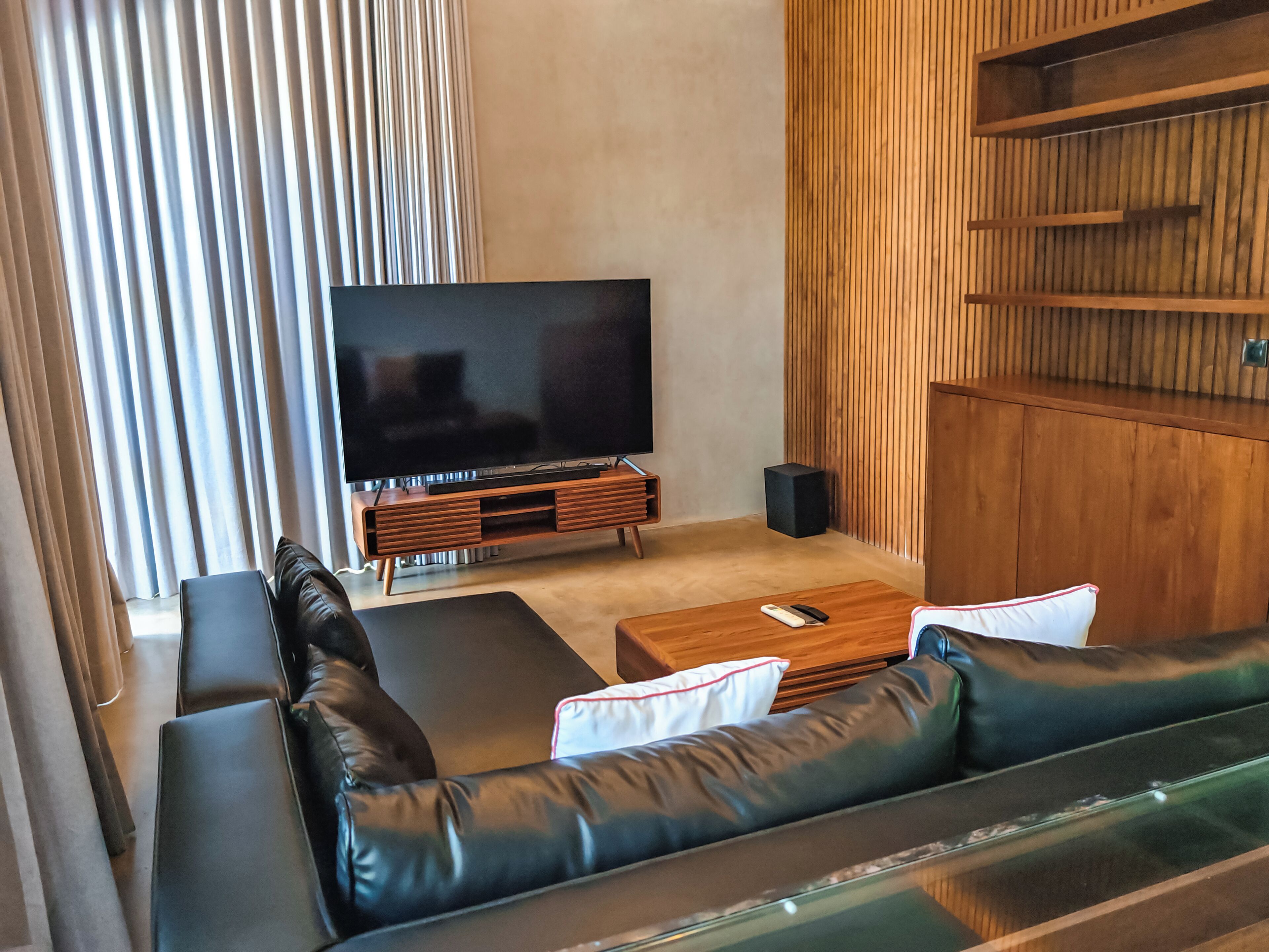 A modern living room with a black leather sofa, a wooden coffee table, and a large flat-screen TV on a wooden stand.