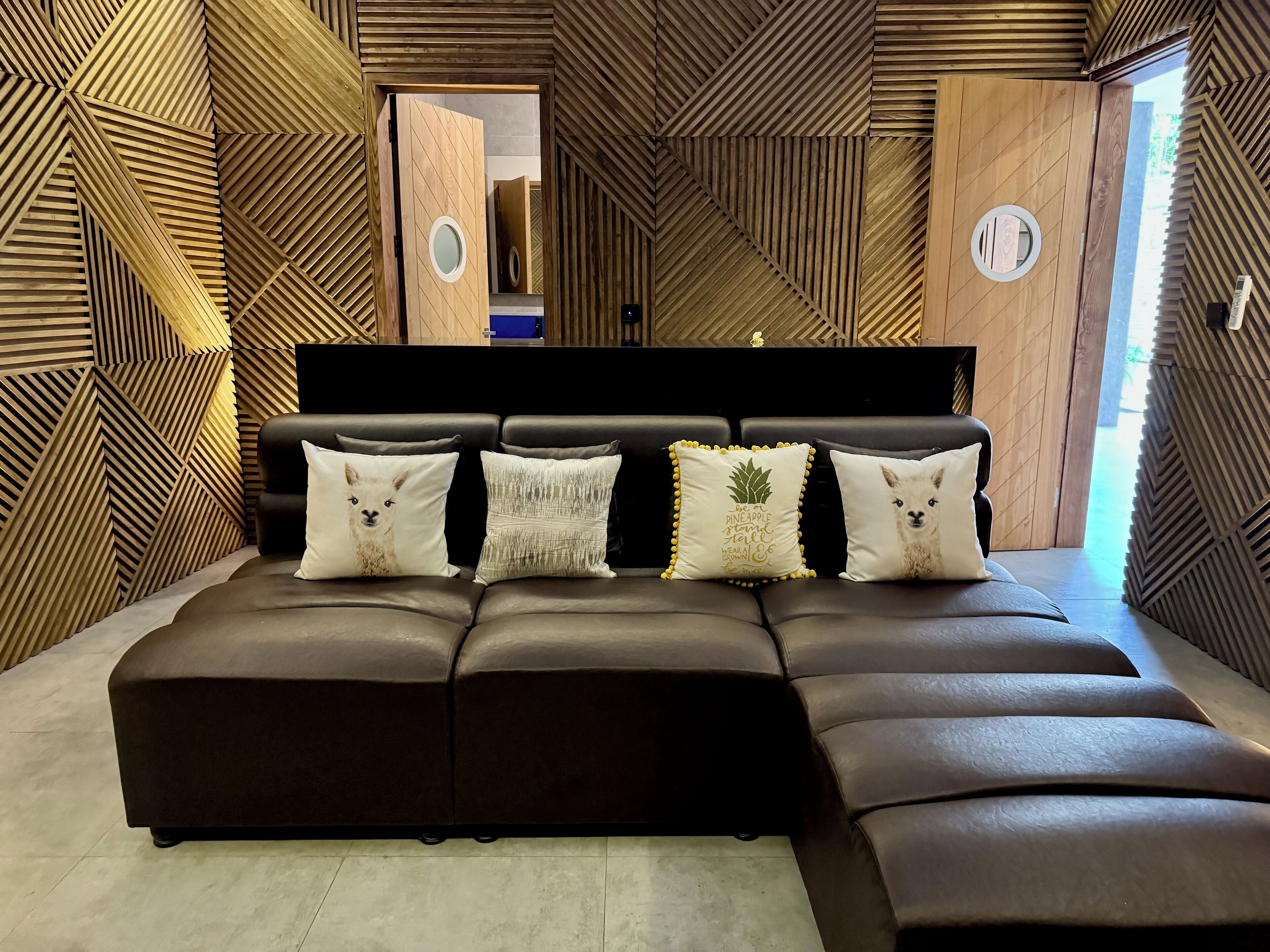 A modern bedroom with a sectional sofa, a wooden geometric wall design, and a large mirror.