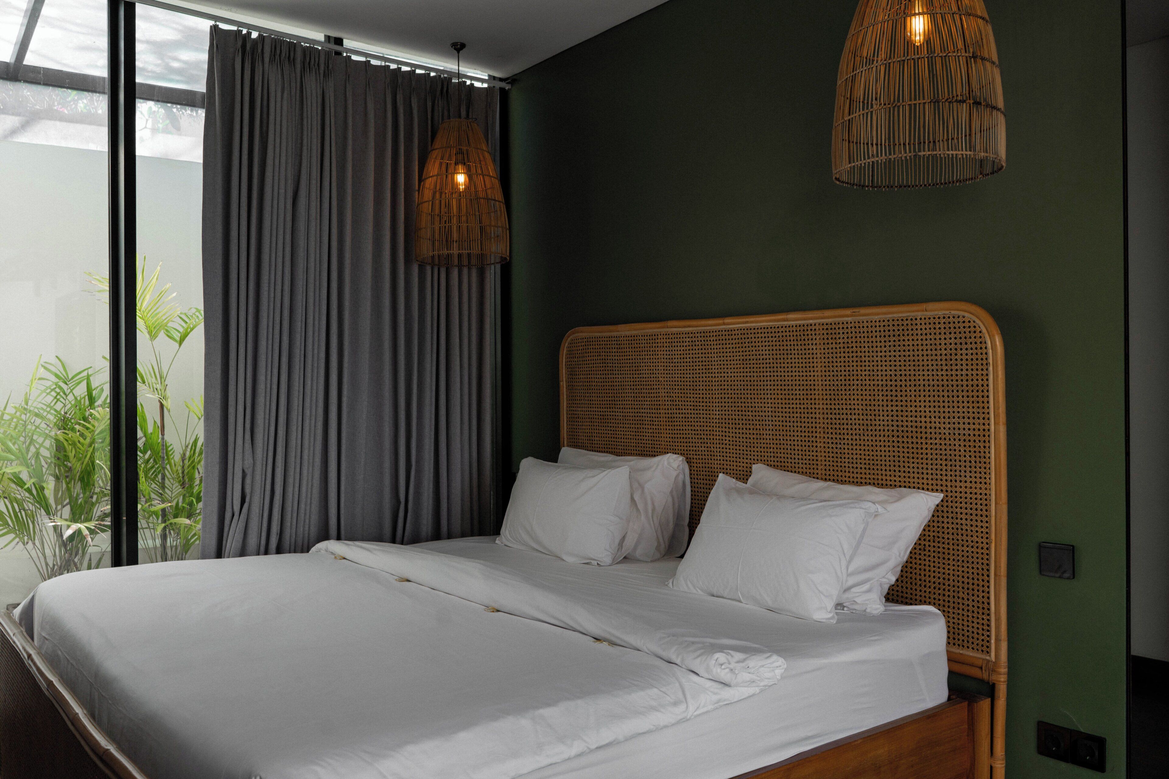 A bed with white linens, a wicker headboard, and two hanging wicker lamps.