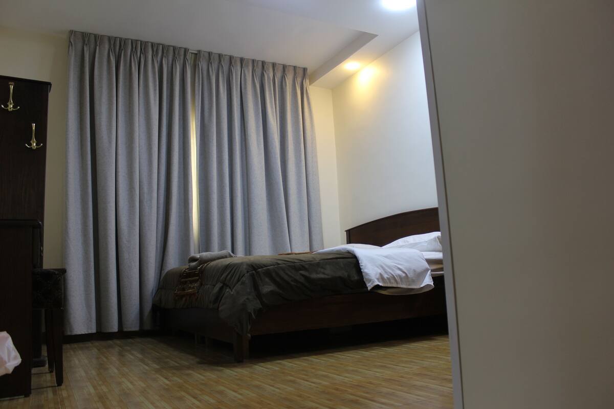 A bedroom with a bed, curtains, a wooden wardrobe, and a nightstand.