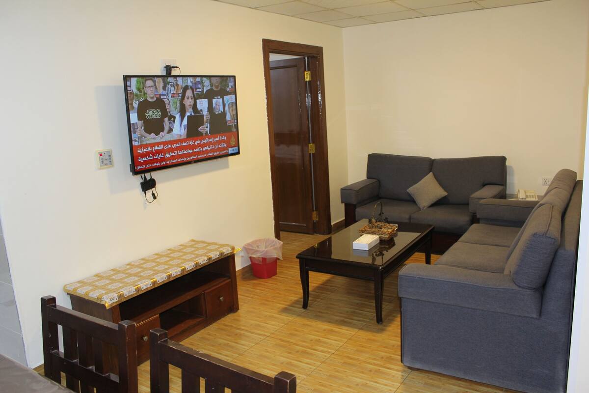 A living room with a television mounted on the wall, a sofa, a coffee table, and a bench.