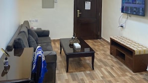 A living room with a sofa, a coffee table, a TV mounted on the wall, and a door with a sign. - Al Ahfad Hotel Apartments  (Amman)