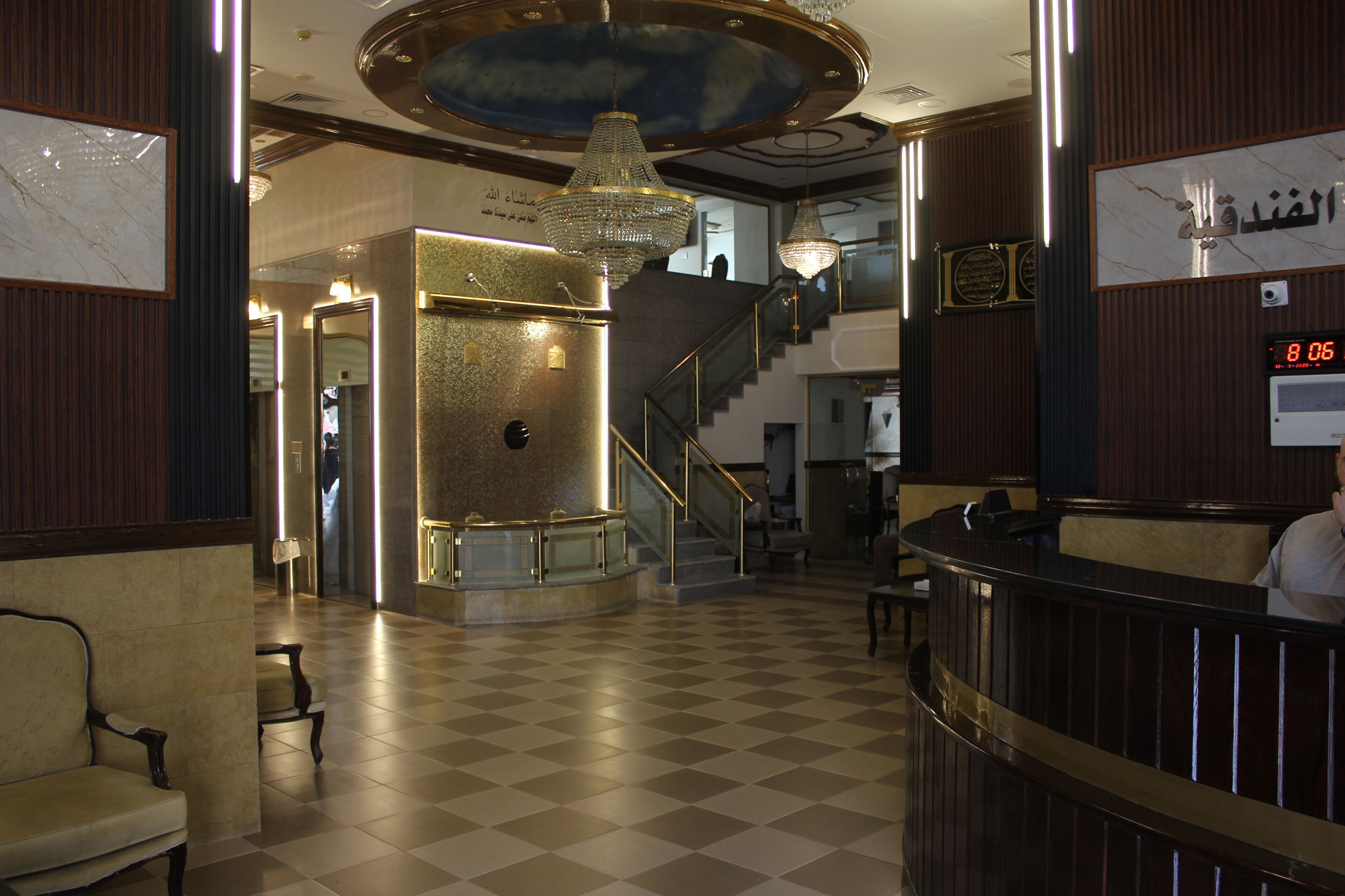 A lobby with a checkered floor, a reception desk, a staircase, and a chandelier.