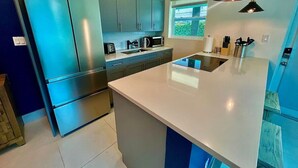 A modern kitchen with stainless steel appliances, a large island, and blue cabinetry. - MiamiVice Las Olas Near Beach & Park with Fire Pit! (Fort Lauderdale)