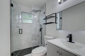 A modern bathroom with a glass shower enclosure, a white toilet, a white sink with a black faucet, and a mirror above the sink.