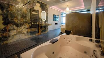 A modern bathroom with a large bathtub, a glass shower enclosure, and a marble wall.