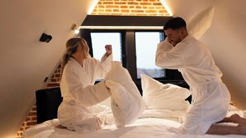 Ein Zimmer mit schrägem Dach, einer Ziegelwand und einem Bett mit weißer Bettwäsche.