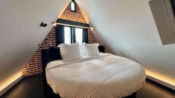 Un dormitorio con techo inclinado, pared de acento de ladrillo y cama con ropa de cama blanca.