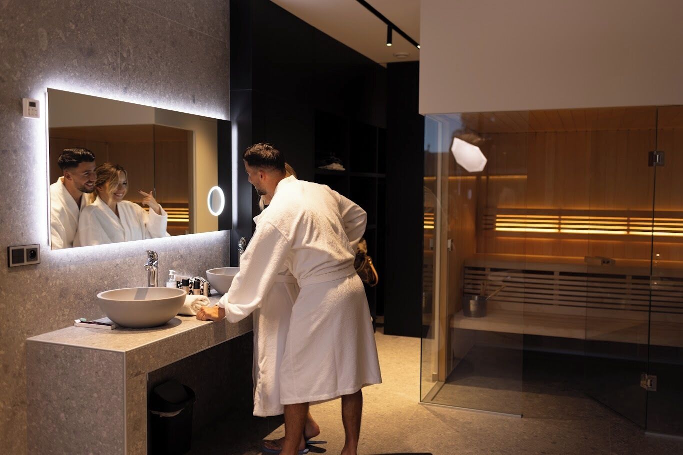 Un baño moderno con un espejo grande, un lavamanos y una zona de ducha con mampara de cristal.